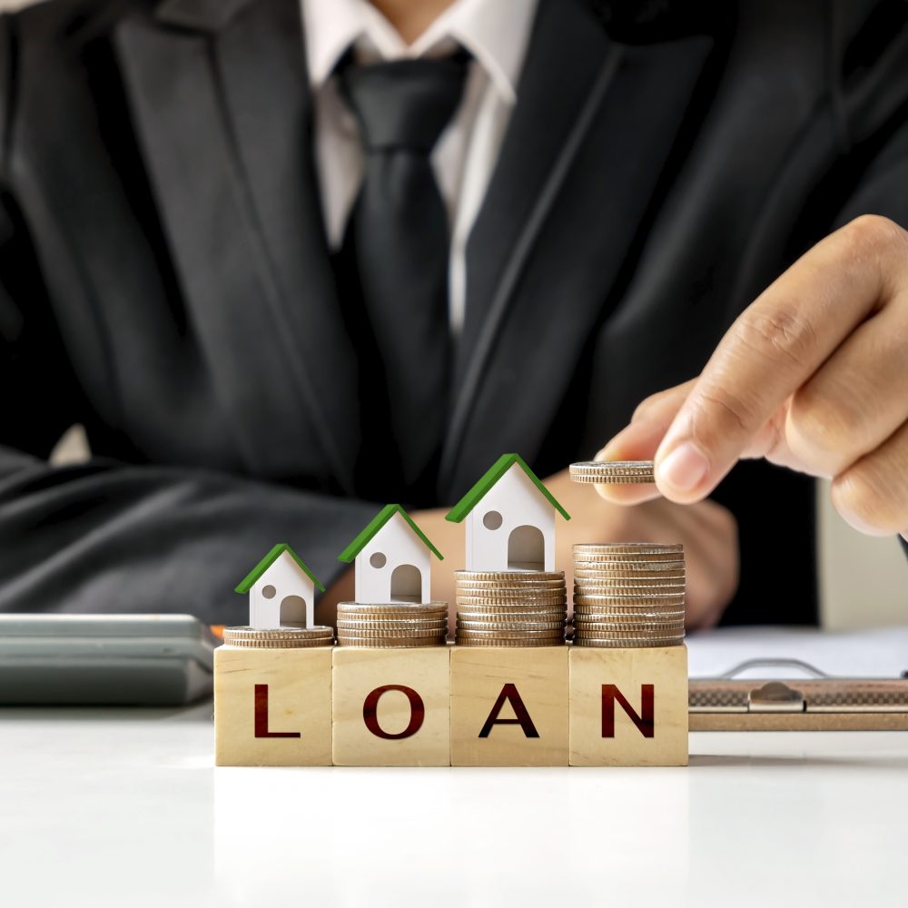 Model house on a pile of coins and businessman holding coins Real estate investment ideas and home loans, new home loans, low-interest rates on homes.